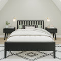 Modern minimalist bedroom with black wooden bed frame, white bedding and pillows, matching black nightstands, wall sconces, potted plant and geometric area rug