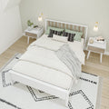 Scandinavian minimalist bedroom with white wooden bed frame, neutral bedding, green and black patterned pillows, matching nightstands, wall sconces and geometric rug