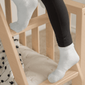 Close-up of baby feet in white socks and black leggings resting on a wooden crib rail in a neutral nursery