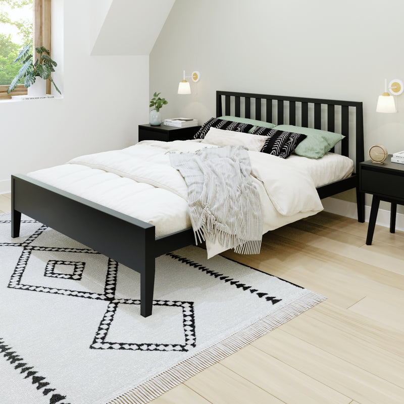 Modern minimalist bedroom with black slatted bed, white bedding, green accent pillows, geometric rug and wood nightstand