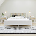 Minimalist Scandinavian bedroom with white wooden bed and slatted headboard, matching nightstands, wall sconces, green plant, bedside clock and black-and-white geometric rug
