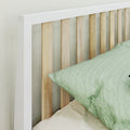 Modern white-framed wooden slat headboard with natural wood slats and green linen pillow on bed, minimalist bedroom decor