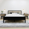 Modern minimalist bedroom with black-framed wooden slat bed, white bedding, patterned pillows, nightstands with lamps and geometric rug
