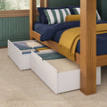 Solid wood canopy bed with navy bedding, green-striped pillows and mustard knit throw on carpet, showing white under-bed storage drawers