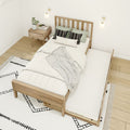 Scandinavian minimalist bedroom with wooden slat bed and pull-out trundle, white bedding and patterned pillows, wooden nightstand with plant and magazine, modern wall sconces, neutral boho rug