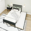 Modern minimalist bedroom with black platform bed and pull-out trundle, white bedding, black nightstand, wall sconces, light wood floor and patterned rug