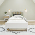 Minimalist bedroom interior with white wooden bed, green and patterned pillows, white nightstand with vase and books, and modern wall sconces on neutral walls