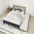 Modern Scandinavian bedroom featuring a black wood trundle bed with white bedding and a gray throw, green and patterned accent pillows, wood-and-black nightstand with plant and magazines, wall-mounted sconces and geometric rug on light hardwood floor.