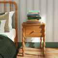 Wooden turned-leg bedside nightstand with stacked books next to bed with green quilt and textured pillows in a cozy farmhouse bedroom
