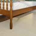 Close-up of solid wood spindle bed frame and white mattress on hardwood floor with beige rug and green bolster pillow visible