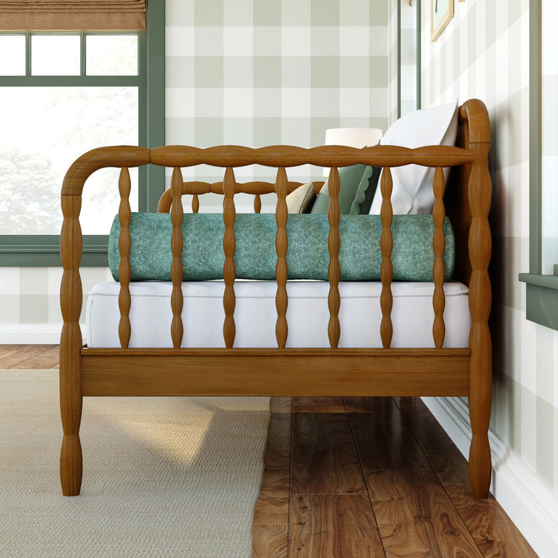 Spindle wooden crib, teal bolster and white bedding in sunlit green-trim nursery with gingham wallpaper and hardwood floor