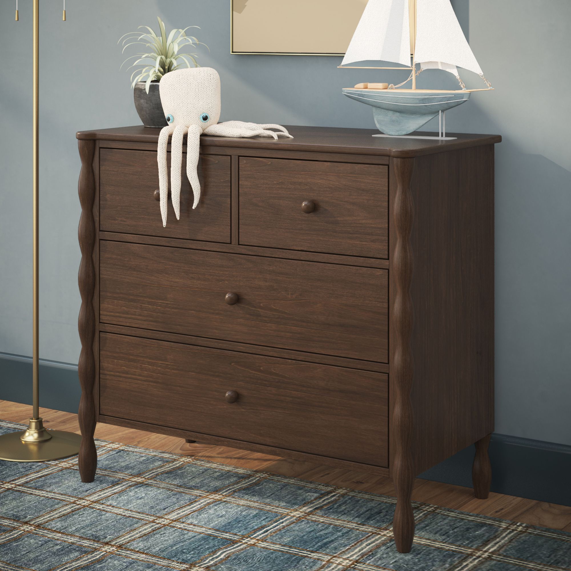 A dark finish Jenny Lind style dresser with 4 drawers in a blue room. A white octopus toy, sailboat, and plant are on top of the dresser.
