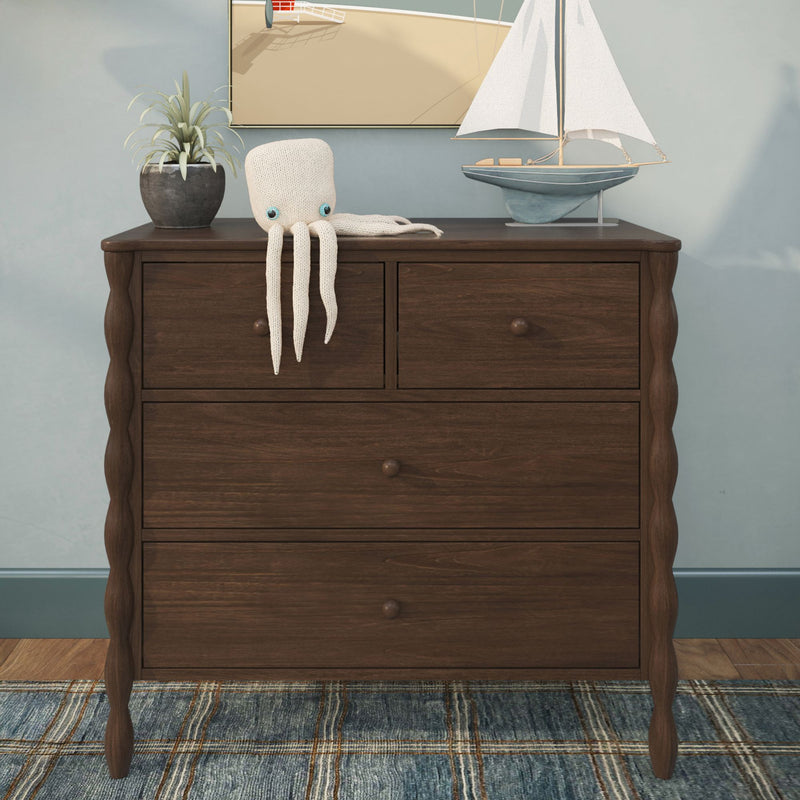 Dark wood dresser styled with knitted octopus toy draped over edge, blue model sailboat, potted plant and coastal nursery decor wall art