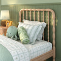 Green kids bedroom with light wood spindle headboard, green striped bedding, plush octopus toy, rattan lamp and wooden toy