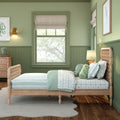 Green children's bedroom with wooden twin bed, mint and white striped bedding, patterned bolster pillow, plush sea creature toy, roman window shades, framed ocean print and wicker bedside lamp