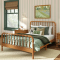 Cozy children's bedroom interior with wooden spindle bed, green quilted bedding, striped wallpaper, bedside table with lamp and framed artwork