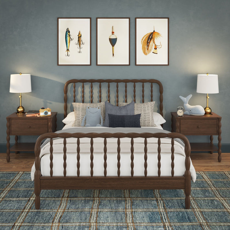Cozy coastal bedroom with wooden spindle bed, blue-gray accent wall, three framed fishing prints above the headboard, bedside lamps, patterned blue plaid rug, decorative pillows and plush toys