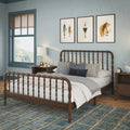 Cozy coastal bedroom with wooden spindle bed, seafoam-blue walls, layered neutral bedding and pillows, plaid blue area rug, nightstand with lamp and alarm clock, and three framed nautical prints above the headboard