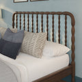 Close-up of a dark wooden spindle headboard with layered white and patterned bedding and blue textured pillows in a cozy farmhouse bedroom