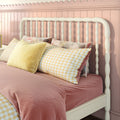 White spindle headboard on pink beadboard wall with pastel pink duvet, yellow gingham pillows and floral throw in cozy nursery