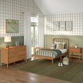 Cozy children's bedroom with wooden spindle bed, sage green wainscoting, beige gingham wallpaper, wooden dresser, nightstand, window with sheer curtains