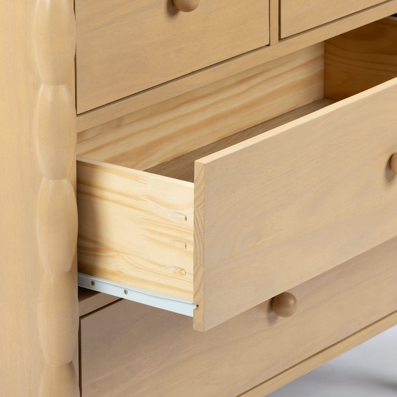 Close-up of light pine dresser with partially open drawer, visible wood grain, round wooden knob and metal drawer slides — natural finish bedroom storage furniture