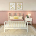 Pastel pink girls nursery with white spindle bed, yellow gingham bedding, scalloped wainscoting, floral framed prints, bedside lamp and plush toys