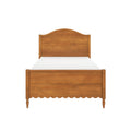 Solid wood bed frame with curved headboard, scalloped footboard and turned legs in a warm natural finish, mattress visible, isolated on white background