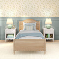 Pastel bedroom interior with wooden twin bed and scalloped headboard, floral wallpaper accent, mint bedside lamps, white nightstands and decorative pillows