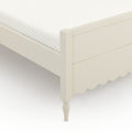 Close-up of white quilted mattress topper on cream wooden bed frame with scalloped skirt and turned leg, minimalist bedroom furniture