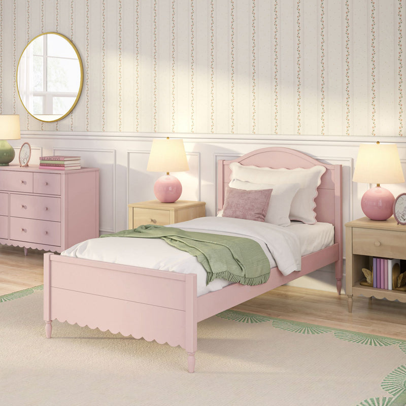 Pastel pink girl's bedroom with scalloped wooden bed, green throw, pink dresser, bedside lamps, round gold mirror and floral striped wallpaper
