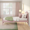 Pastel pink bedroom interior with tufted bed, green knit throw, pink nightstand, bedside lamp, sheer curtains and gold round mirror
