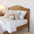 Cozy girl's bedroom with wooden twin bed, pastel pink bedding, floral throw pillows, plush teddy bear and bedside lamp against floral wallpaper