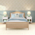 Cozy coastal cottage bedroom with light wood bed, blue and white pillows, floral wallpaper and mint ceramic bedside lamps on white nightstands