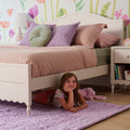 Cozy girls' bedroom with white bunk bed, pastel pink bedding, round green cushion, floral wallpaper and purple shag rug — kids' room decor inspiration