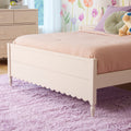 Pastel girls' bedroom with white scalloped twin bed, pink textured bedding, round green and lavender pillows, plush purple shag rug, floral wall decals and teddy bear