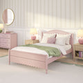 Pastel pink bedroom interior with scalloped wooden bed, white bedding and pink pillows, green throw blanket, bedside lamps, pink dresser, round mirror and floral striped wallpaper