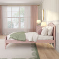 Pastel pink bedroom with pink bed frame, green throw blanket, layered sheer curtains, bedside lamp, round mirror and subtle patterned wallpaper