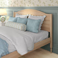 Cozy pastel bedroom interior: light wood headboard, scalloped white-and-blue pillows, striped floral bolster, blue throw blanket and bedside lamp
