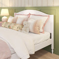 Cozy white wooden twin bed with pink pillows, floral bolster and teddy bear against green wainscoting and floral wallpaper, nursery bedroom decor