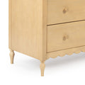 Close-up of a light wood three-drawer bedside table (nightstand) with round wooden knobs, turned legs, scalloped apron and natural finish