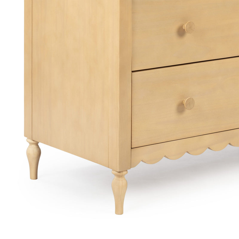 Close-up of a light wood three-drawer bedside table (nightstand) with round wooden knobs, turned legs, scalloped apron and natural finish