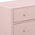 Close-up of blush pink wooden dresser top and drawers with round knob, modern nursery storage cabinet