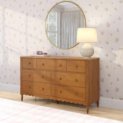 Wooden six-drawer dresser in bedroom with round gold mirror, ceramic table lamp, pink headphones and delicate floral wallpaper