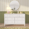 White dresser with round gold-framed mirror, pink table lamp, green headphones and wooden toy houses against vintage floral wallpaper and olive wainscoting — cozy nursery bedroom decor
