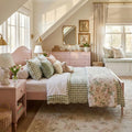 Cozy pink cottagecore children's bedroom with pink bed frame, green gingham bedding, floral quilt, pastel pillows, window seat, vintage dresser and scalloped mirror