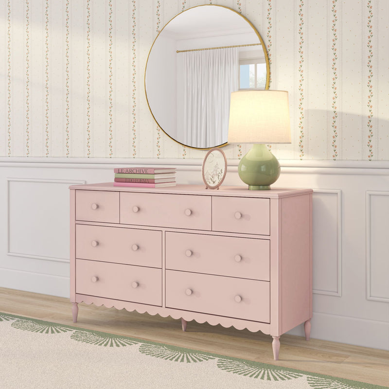 Pink shabby-chic dresser with round gold mirror, green ceramic lamp, stacked books and floral striped wallpaper in a feminine bedroom