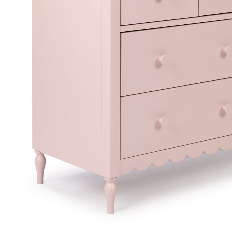 Light pink wooden dresser with four drawers, round knobs, scalloped base and turned legs for nursery or bedroom storage