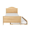 Light wood twin bed frame with arched headboard, scalloped footboard, turned legs and under‑bed trundle storage shown with white mattress — space‑saving kids' bedroom or guest room furniture