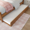 Wood trundle bed with pull-out mattress, white bedding and pale pink throw on hardwood floor